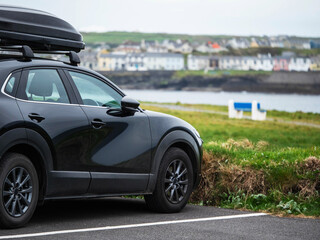 Black car with black cargo box is parked in a car park with view on the ocean and beautiful scenery...