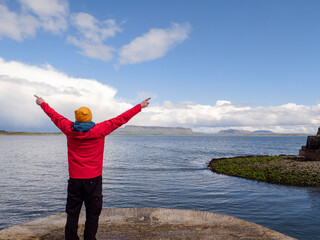 Male tourist in yellow hat and red jacket is standing on a pier and looking at ocean and Benbulbin...