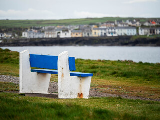 Blue and white benches on a grass with view on ocean and white houses on other side of bay....