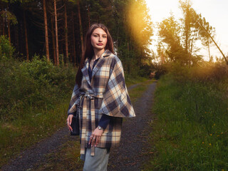 A woman is standing on a dirt road wearing a vogue style jacket and blue jeans. She is looking at...