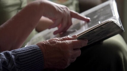 Elder grandmother and young granddaughter looking through vintage photo album, sharing cherished family memories. Spending time with family. Visiting elderly in nursing home. Communication loved ones