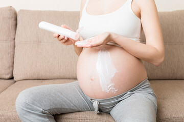 pregnant woman applying stretch mark cream to belly. pregnancy, people and maternity concept....