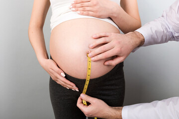 happy beautiful pregnant young woman touching her bare tummy while a doctor is measuring it