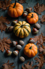 Vibrant pumpkins in shades of orange and green are arranged among fallen autumn leaves and acorns on a rustic wooden table