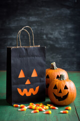 Two carved pumpkins with playful faces sit beside a black bag filled with candy on a green table, creating a festive Halloween atmosphere