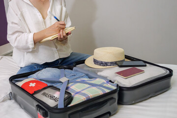 making a check list of things to pack for travel. woman writing checklist item on notebook and...