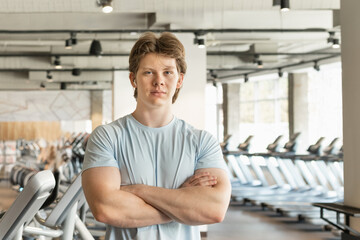Portrait of caucasian handsome fitness coach standing wearing blue t-shirt with cross hand at gym....