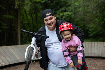 Happy father carrying smiling daughter while holding a balance bike after a successful training...