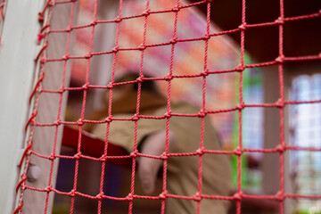 A child plays in a maze in a playroom A child happily plays behind a bright red safety net in a...