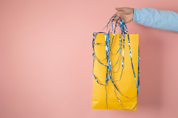 Male hand wearing a blue sweatshirt holding a yellow shopping bag with blue confetti overflowing on...