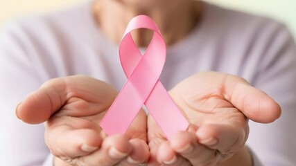 Elderly woman's hands gently cradling a pink ribbon, symbol of breast cancer awareness. - Powered by Adobe