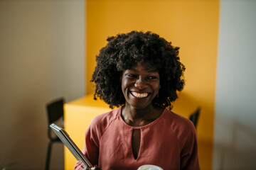 Smiling black woman holding laptop and coffee in modern office