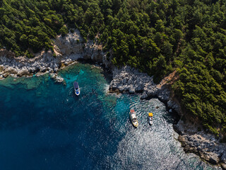 Aerial view of turquoise sea with boats near rocky coast and forest in Alanya, Turkey. Summer drone footage of scenic Mediterranean shoreline and clear water. Summer holiday in Alanya.