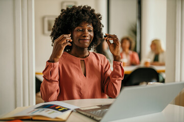 Smiling black woman wearing earbuds working on laptop in office