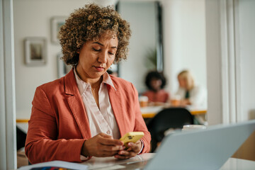 Businesswoman using mobile phone in office with colleagues working in the background