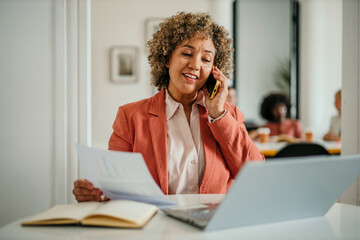 Businesswoman working on laptop and talking on phone in office
