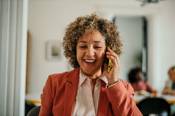 Happy businesswoman laughing while talking on mobile phone in office