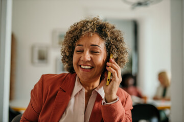 Happy businesswoman laughing while talking on mobile phone in office