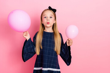 Young girl holding pink balloons, posing in a blue dress against a vibrant pastel pink background,...