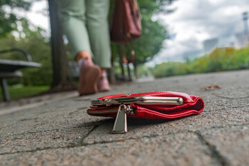 red wallet with money on the sidewalk and a woman walking away. A close-up of a forgotten wallet on the sidewalk tiles.