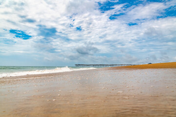 Rustic wooden jetty on wide shoreline. Cloudy summer sky over calm sea and empty coast.