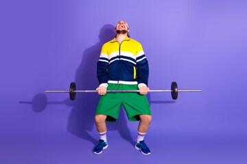 Active man lifting weights in retro sport outfit on purple background, showcasing a vibrant and...