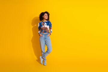 Cheerful young woman with an afro hairstyle standing in casual wear against a vibrant yellow...