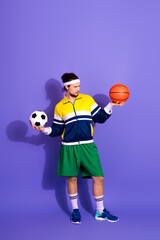 Young sporty man in retro-style activewear holding basketball and soccer ball, posing against a...