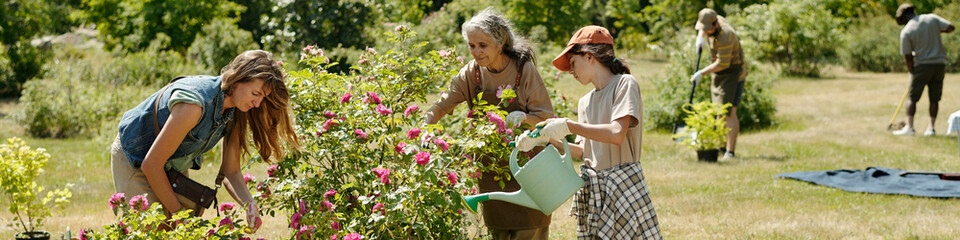 Multiethnic group of middle aged woman, teenager girl, young adult woman and young adult man gardening together outdoors, planting and watering flowers in green park setting © pressmaster