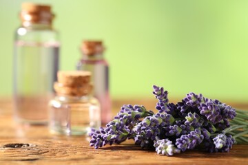 Bottles of lavender essential oil and flowers on wooden table, closeup