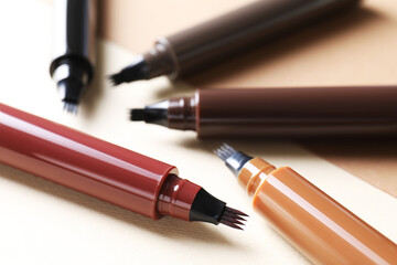 Different liquid eyebrow pencils on beige background, closeup