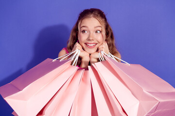 Cheerful young woman with shopping bags on a vibrant purple background showcasing joy for fashion...