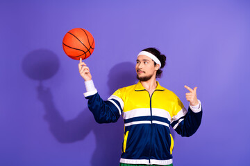 Young man in sportswear spinning a basketball on his finger with a vibrant purple background...
