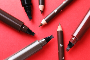 Different eyebrow pencils on red background, flat lay