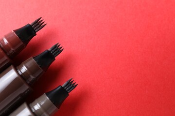Liquid eyebrow pencils on red background, above view. Space for text
