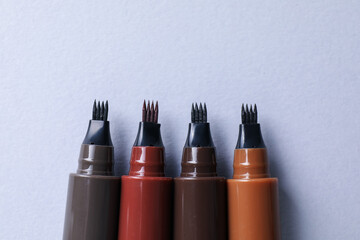 Liquid eyebrow pencils on white background, flat lay