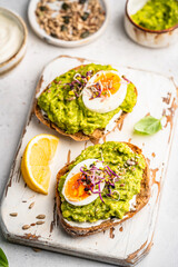 Toast with avocado, feta cheese, eggs, herbs and seeds with lemon slices on white background. Healthy eating and wholesome Breakfast