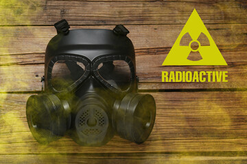 Radiation threat. Gas mask, radioactive sign and smoke on wooden table, top view
