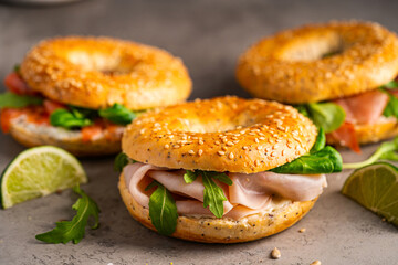 Variety of Bagel sandwiches with ricotta, prosciutto or chicken ham or salmon and microgreens, bagel with ham for breakfast on gray background, close up. Healthy breakfast food.