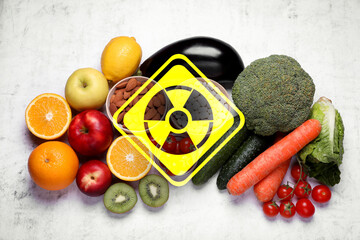 Fresh vegetables and fruits on white table and radioactive sign, top view. Environmental contamination, polluted food