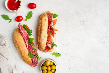 Assorted delicious baguette sandwiches filled with thinly sliced ham or salami and fresh green...