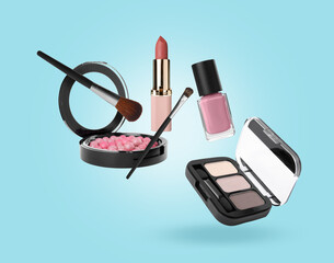 Eyeshadow palette and other makeup products in air against light blue background