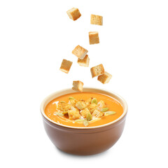 Croutons falling into bowl of creamy pumpkin soup against white background