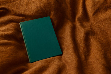 Green blank book on orange textured cloth background
