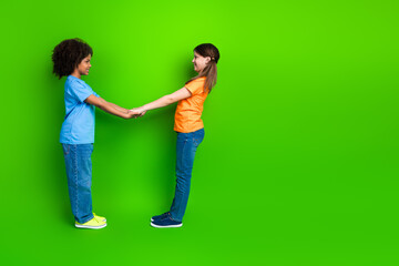 Two school-aged girls interacting joyfully against a vibrant green background, emphasizing friendship and childhood