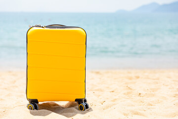 Yellow suitcase stands on white sandy beach with blue sea background. Travel insurance and touristic concept. Summer holidays lifestyle. Copy space. Mock up. High quality photo