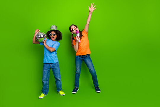 Two cheerful children standing against a vibrant green background, posing with enthusiasm and expressing joy with fun props.
