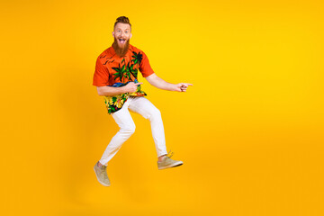 Cheerful red-haired man with a beard, jumping joyfully against a bright yellow background, wearing...