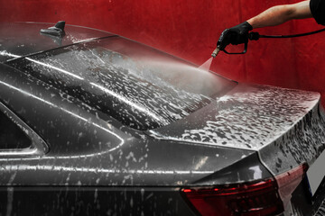Pressure Rinsing Car After Foam Application. Detailed cleaning using pressure hose ensures no foam...