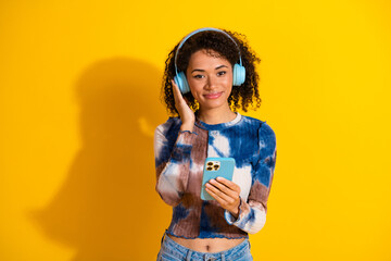 Young woman with headphones enjoying music while using a smartphone against a vibrant yellow...